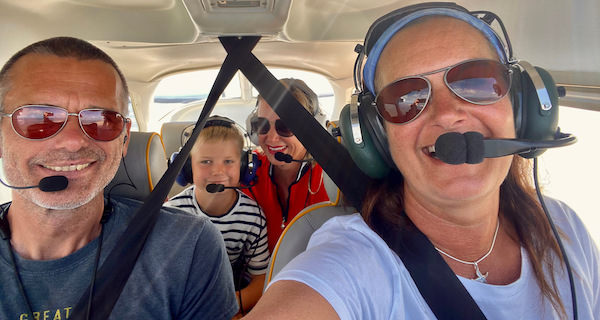 Die Piloten mit Sonnenbrillen fotografieren sich per Selfie während des Rundflugs. Auf der Rückbank sitzt eine Mutter mit Ihrem kleinen Sohn, beide sehen in die Kamera.