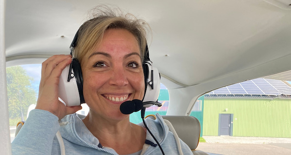 Eine junge Frau testet Ihren weißen Kopfhörer vor Ihrem Rundflug. Sie lacht dabei herzlich.