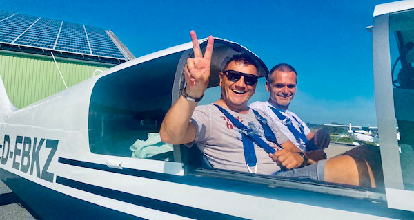 Fluggast vor dem Start im Kleinflugzeug. Er freut sich über sein Geburtstagsgeschenk: ein Rundflug. Im Hintergrund der Pilot. Die Flugzeughaube ist noch nicht geschlossen.