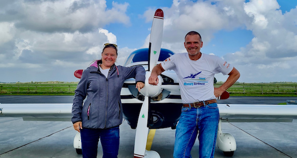 Junge Frau hat Ihren Rundfluggutschein eingelöst und steht lachend mit dem Piloten vor dem Flugzeug.
