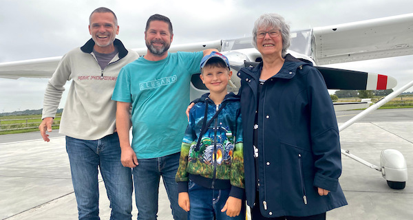 3 Generationen: Mann, seine Mutter und sein Sohn sind über den Nationalpark Wattenmeer geflogen. Sie stehen mit dem Piloten vor dem Flugeug.